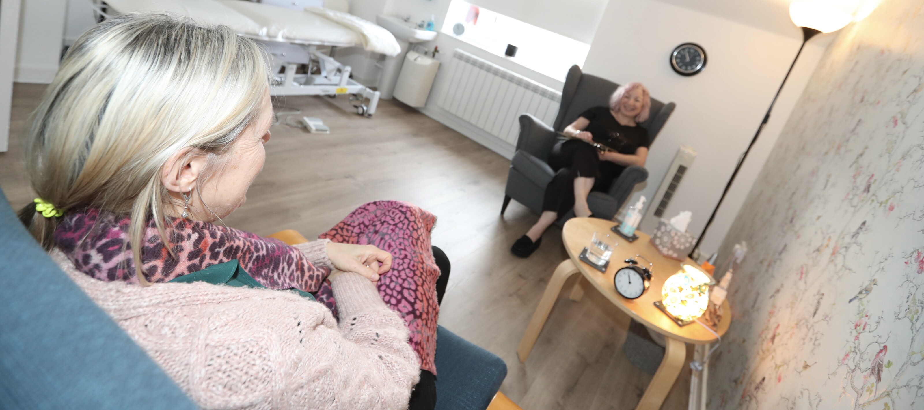 Two practitioners sitting together in conversation in a therapy room with bird wallpaper.