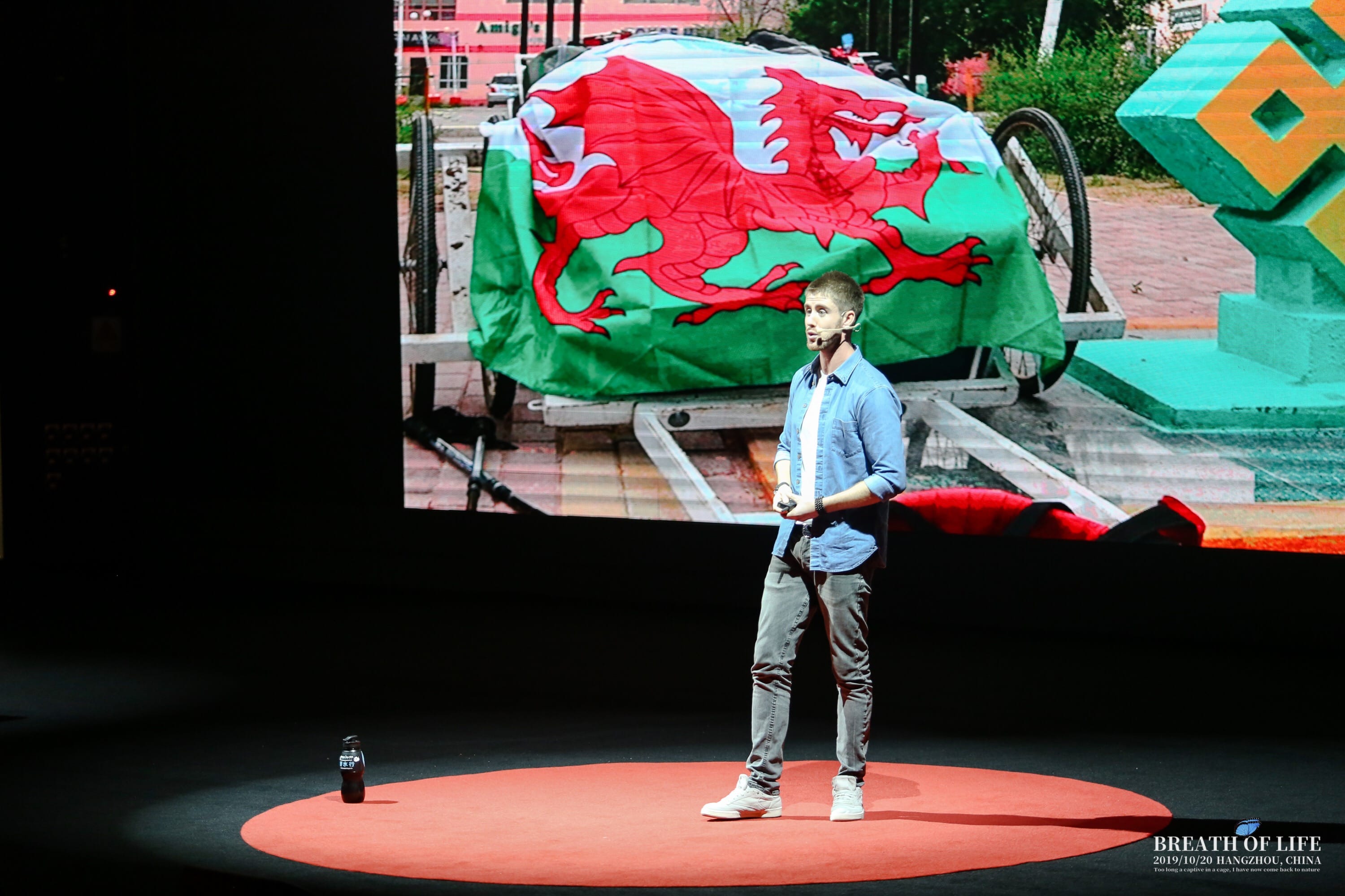Ash Dykes on stage at Breath of Life in Hangzhou, the Mongolia expedition trailer on the screen behind him