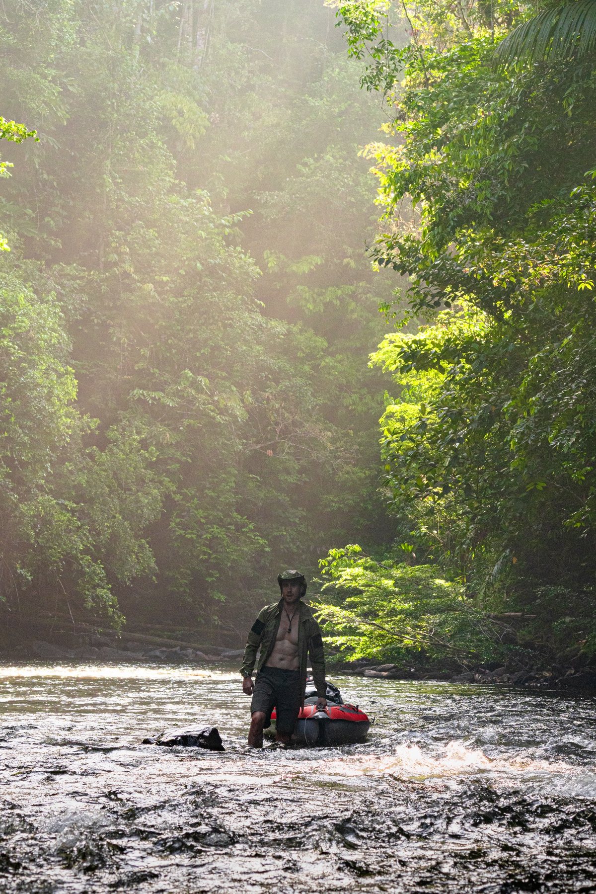 Ash Dykes wading a jungle river, hauling a loaded packraft behind him