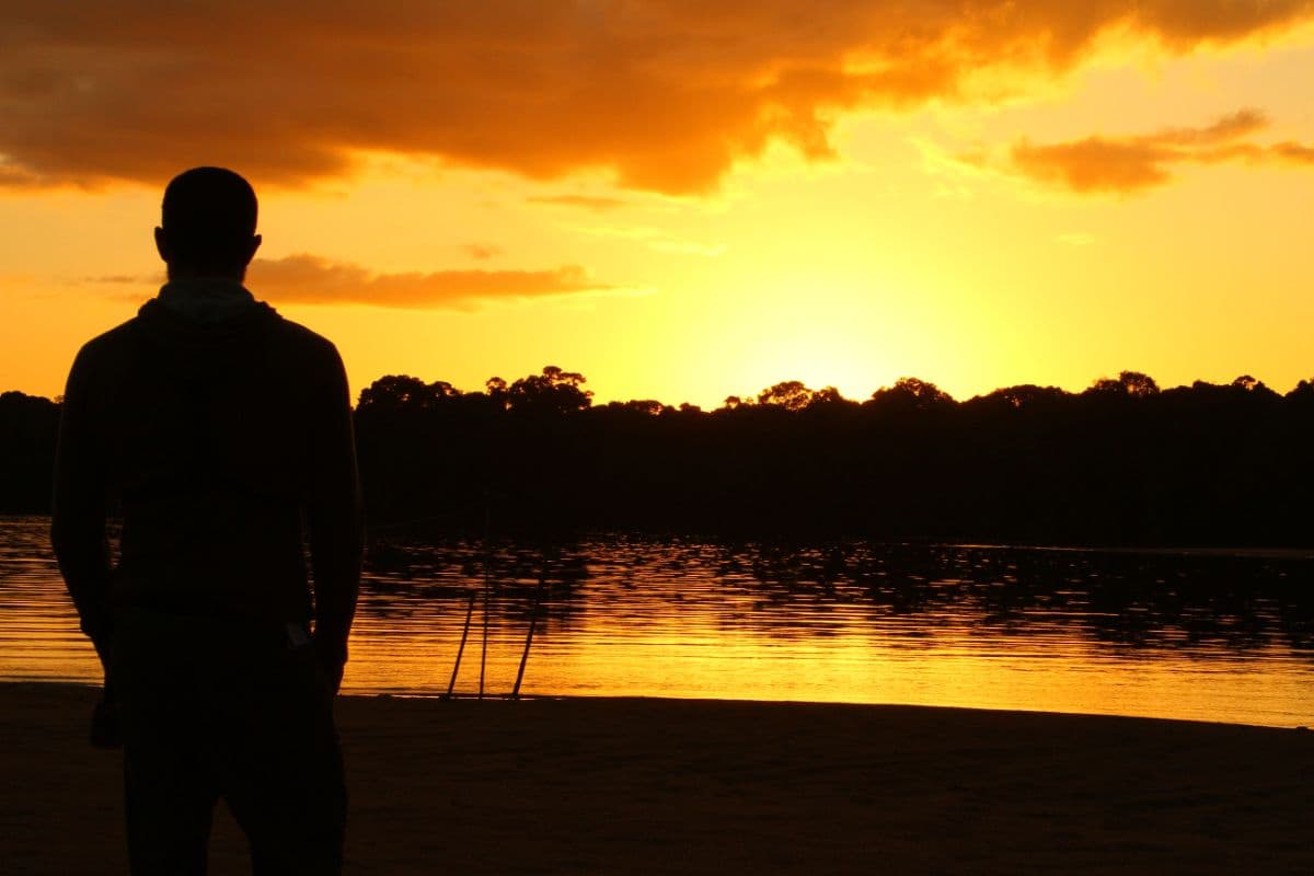 silhouette of a person standing at a lakeside shore watching a golden sunset