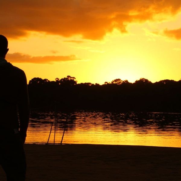 silhouette of a person standing at a lakeside shore watching a golden sunset