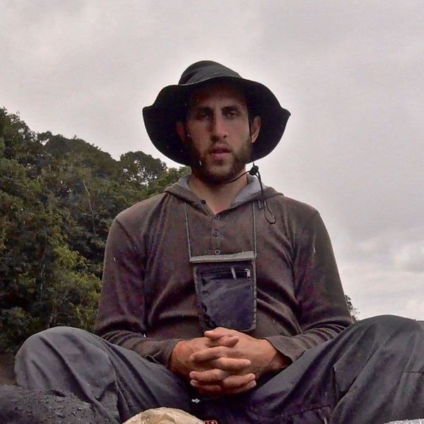 a man in outdoor gear sitting cross-legged on rocky ground in an overcast natural setting
