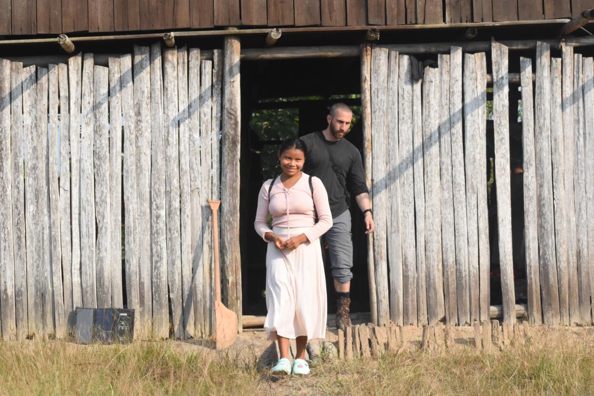 two people emerging from the doorway of a weathered timber building, with a wooden shovel leaning against the wall beside them