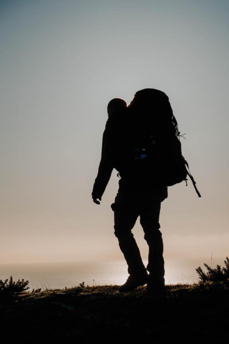 silhouette of a solo hiker with a large pack on a hilltop at dusk