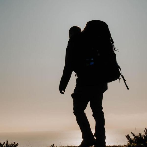 silhouette of a solo hiker with a large pack on a hilltop at dusk