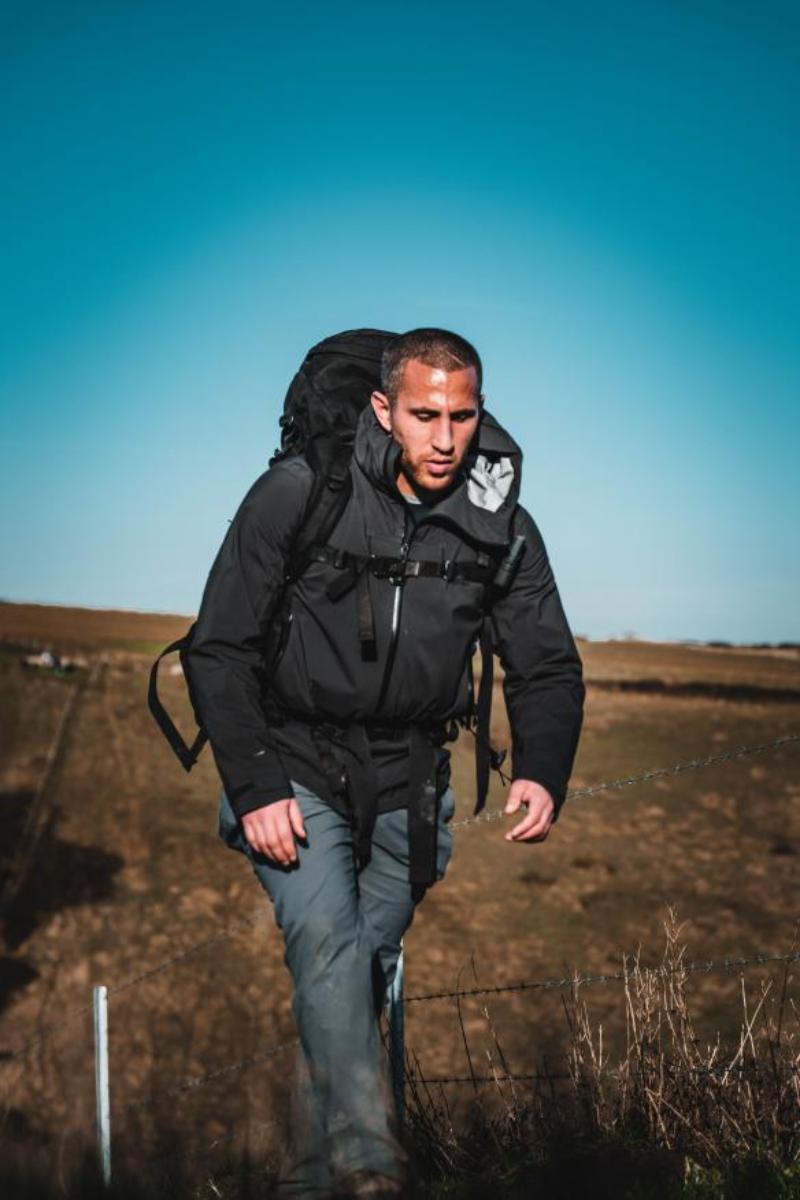a man hiking outdoors with a large backpack along a rural fenced trail