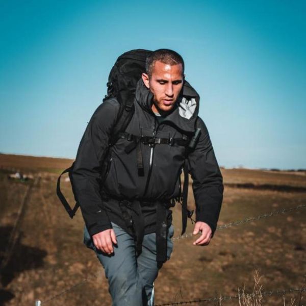 a man hiking outdoors with a large backpack along a rural fenced trail