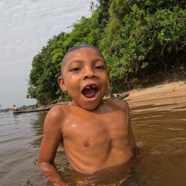 a young child wading and playing in a river, shot at water level with a sandy riverbank and other people visible in the background