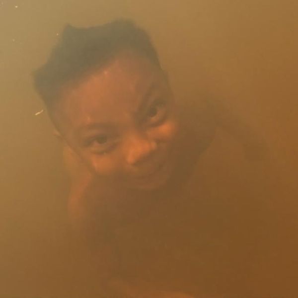 close-up of a person submerged in turbid amber-coloured water, face barely visible through the murk