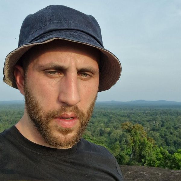 a man wearing an NGS Global Risk Management branded T-shirt at an elevated outdoor viewpoint with a forest canopy in the background