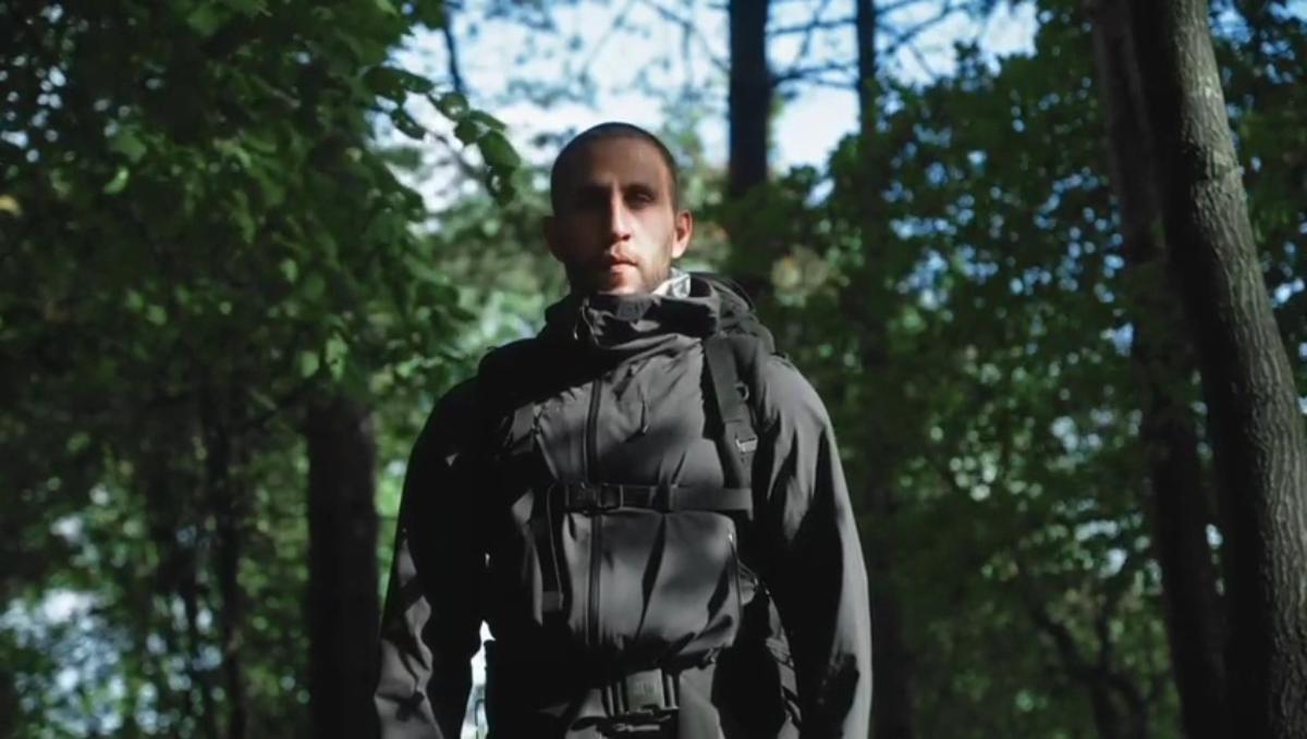 a man in a dark hooded jacket and backpack standing among trees in a forest - outdoor gear lifestyle shot