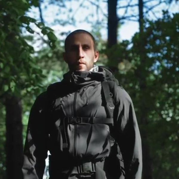 a man in a dark hooded jacket and backpack standing among trees in a forest - outdoor gear lifestyle shot