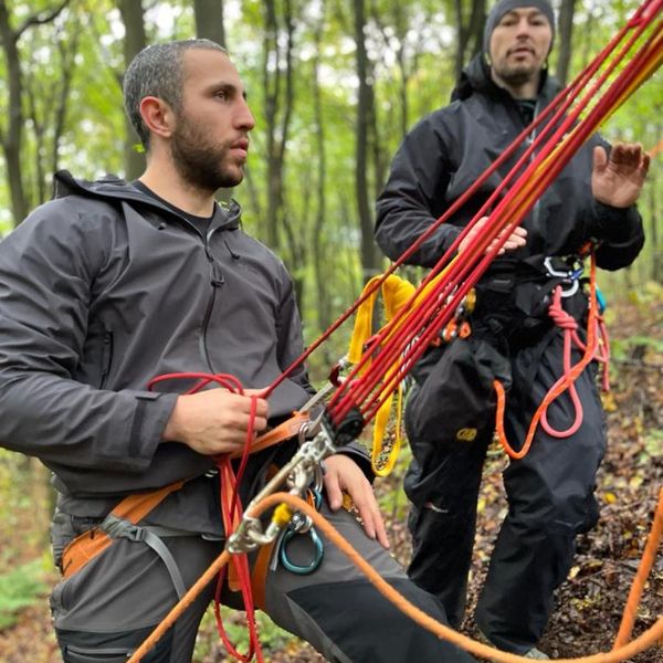 two people in climbing harnesses managing ropes and rigging equipment in a woodland setting