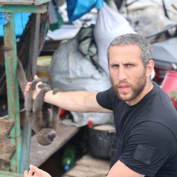 a man holding a small wild animal on a rustic boat, surrounded by sacks and supplies