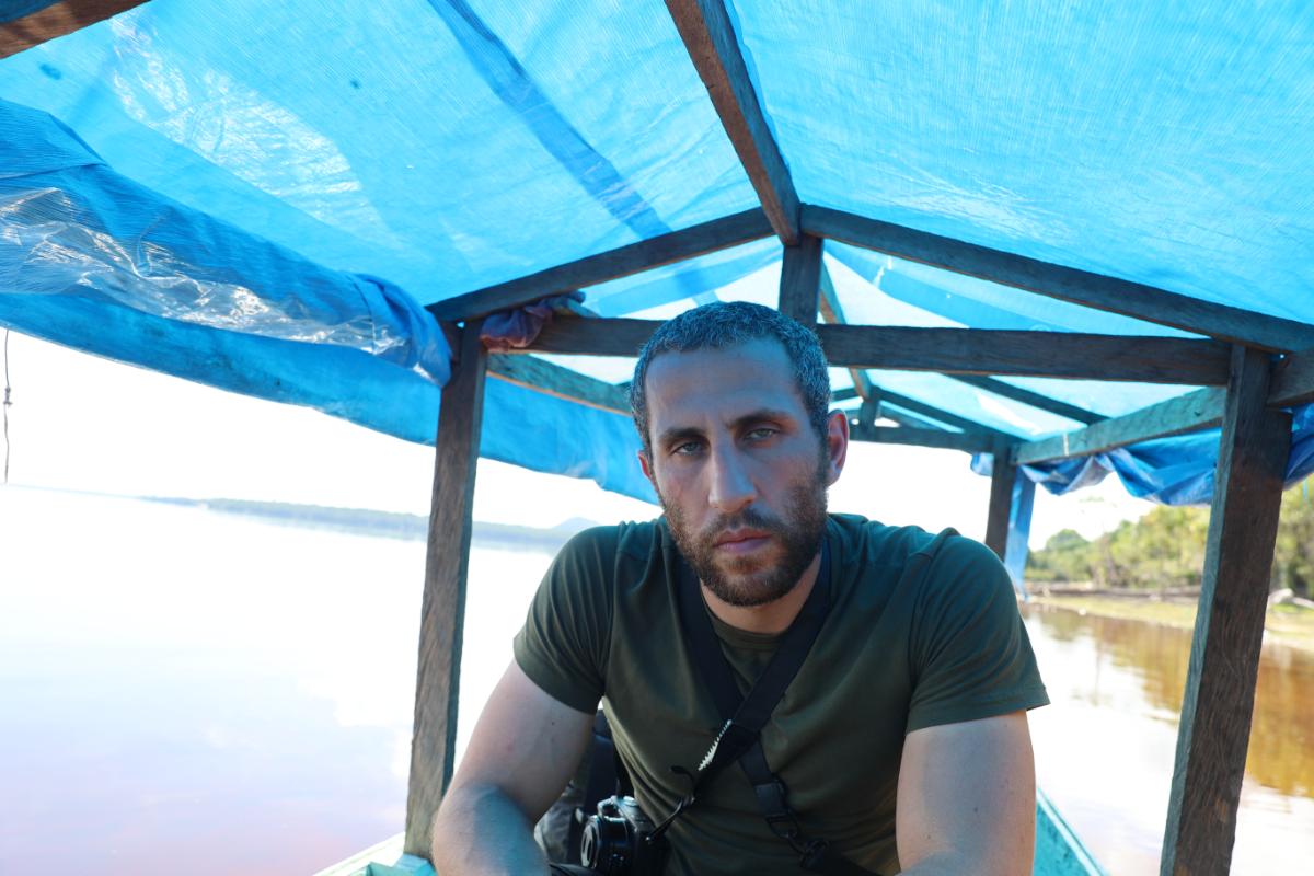 a man with a camera seated under a tarpaulin canopy on a river boat