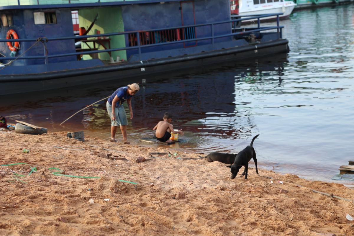 two people and a dog at a riverbank beside a moored vessel