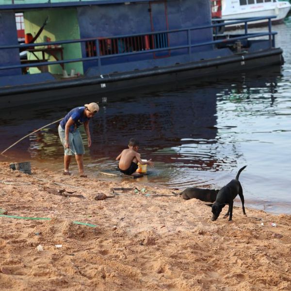 two people and a dog at a riverbank beside a moored vessel